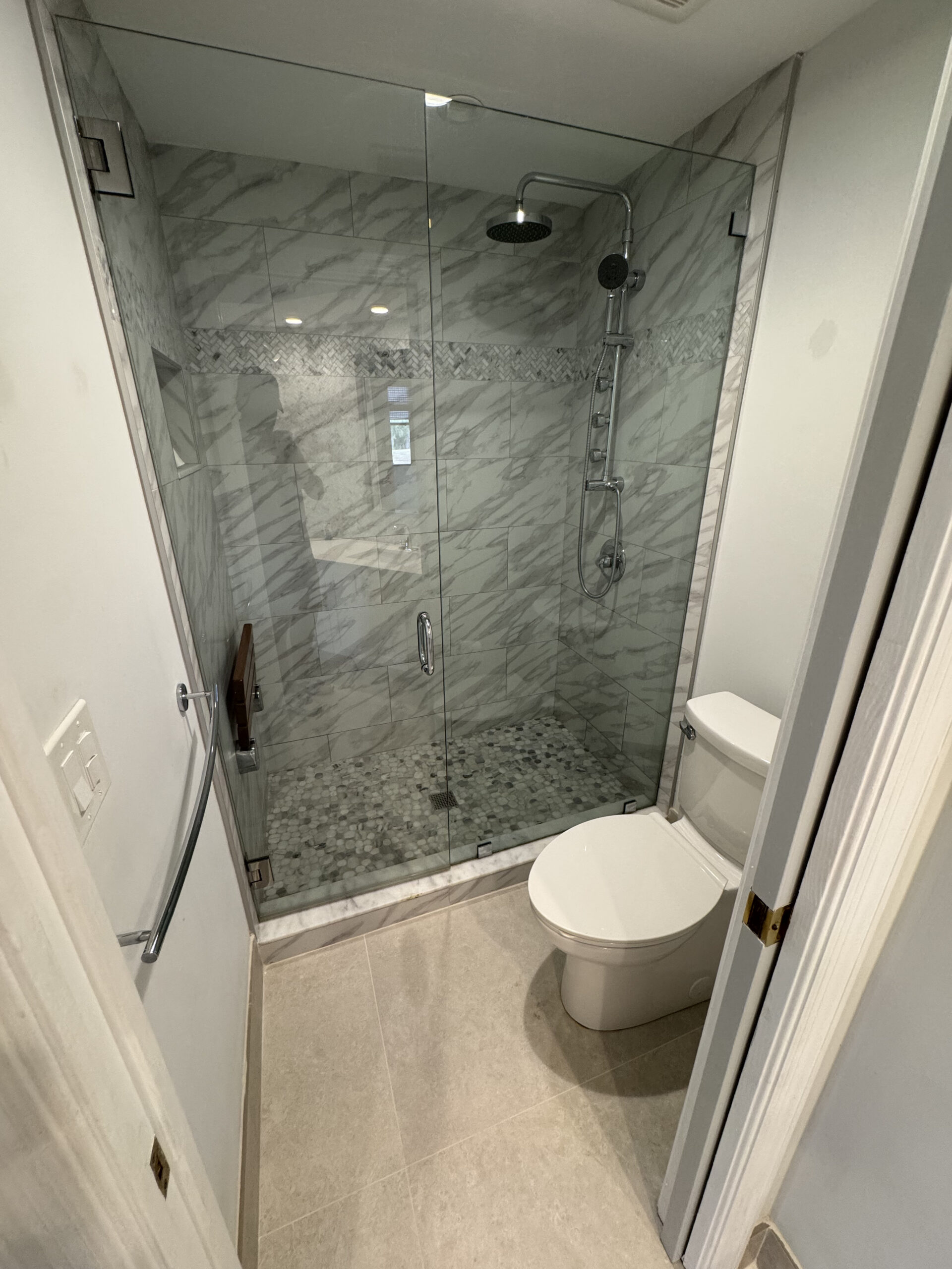 Modern bathroom with a glass-enclosed shower featuring a rainfall showerhead and tile walls, next to a white toilet. Light-colored floor tiles and a sleek, clean design.